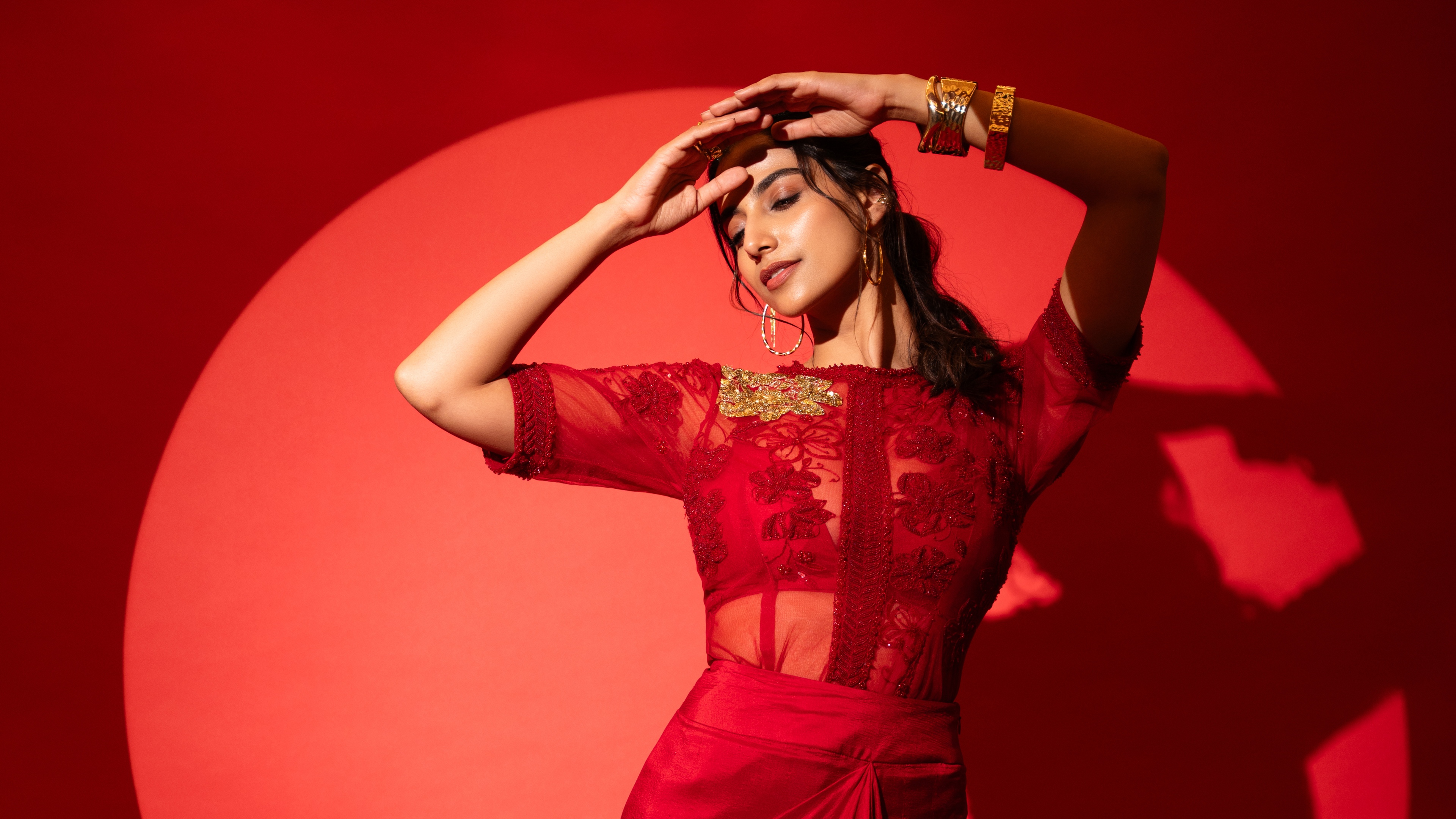 A monochromatic red-themed portrait of Indian actress Meenaakshi Chaudhary wearing an elegant red dress.