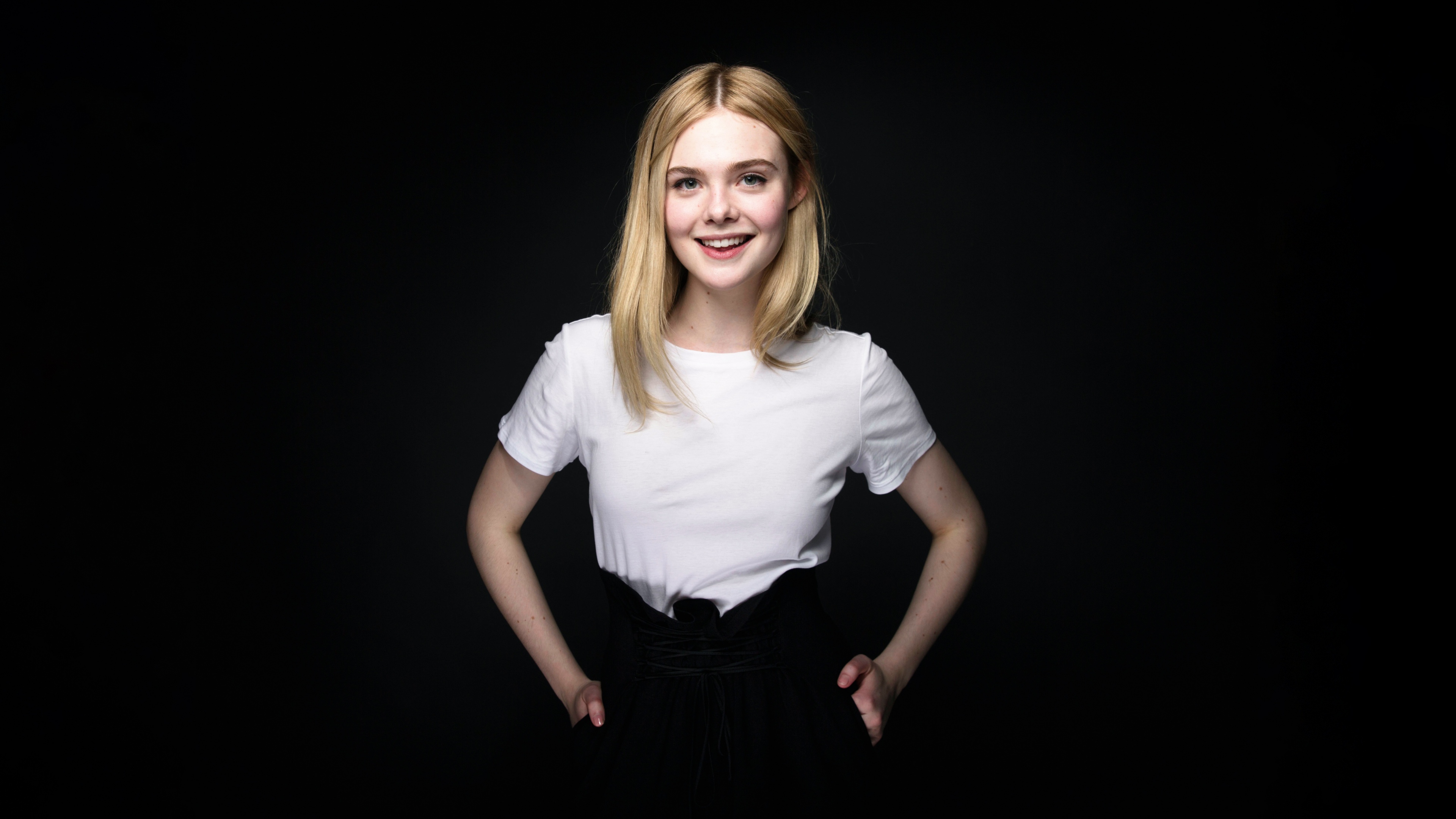 A close-up portrait of a smiling blonde actress, Elle Fanning, against a dark background