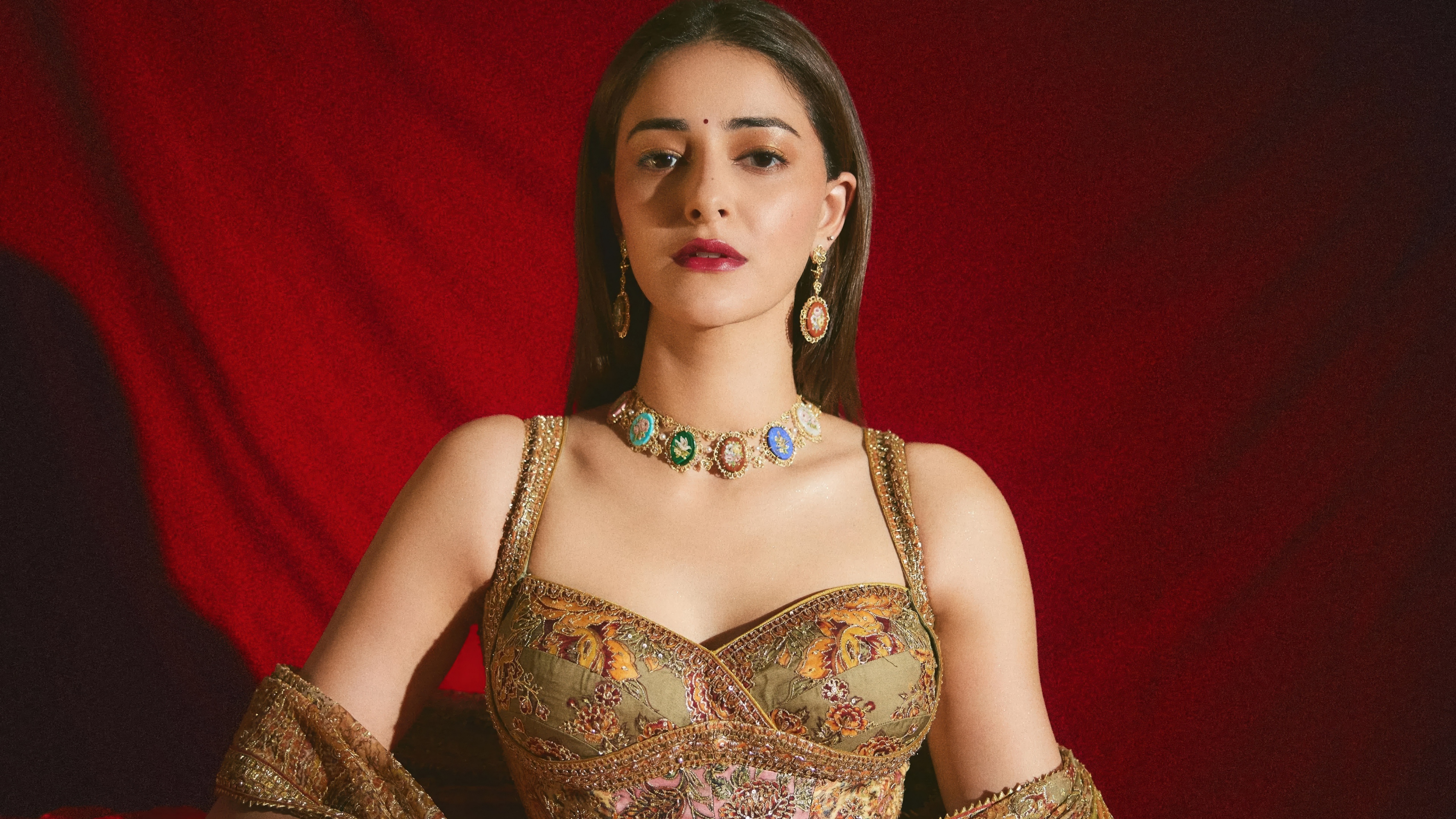 Ananya Panday wearing traditional Indian clothing against a vibrant red background.