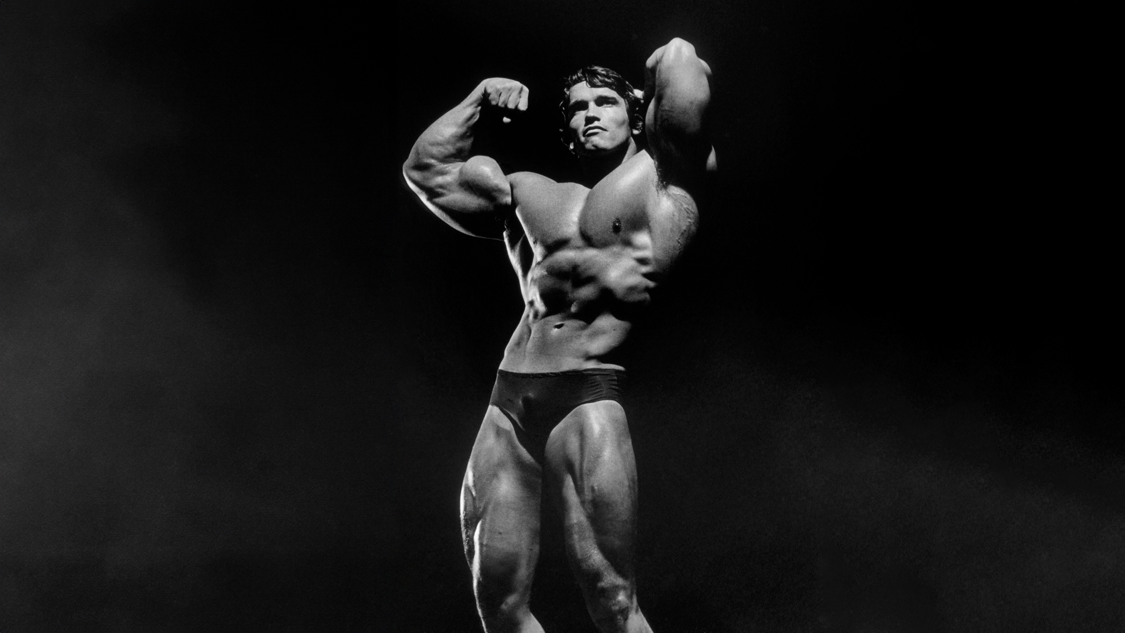 A high-contrast monochrome portrait of Arnold Schwarzenegger showcasing his bodybuilding physique.