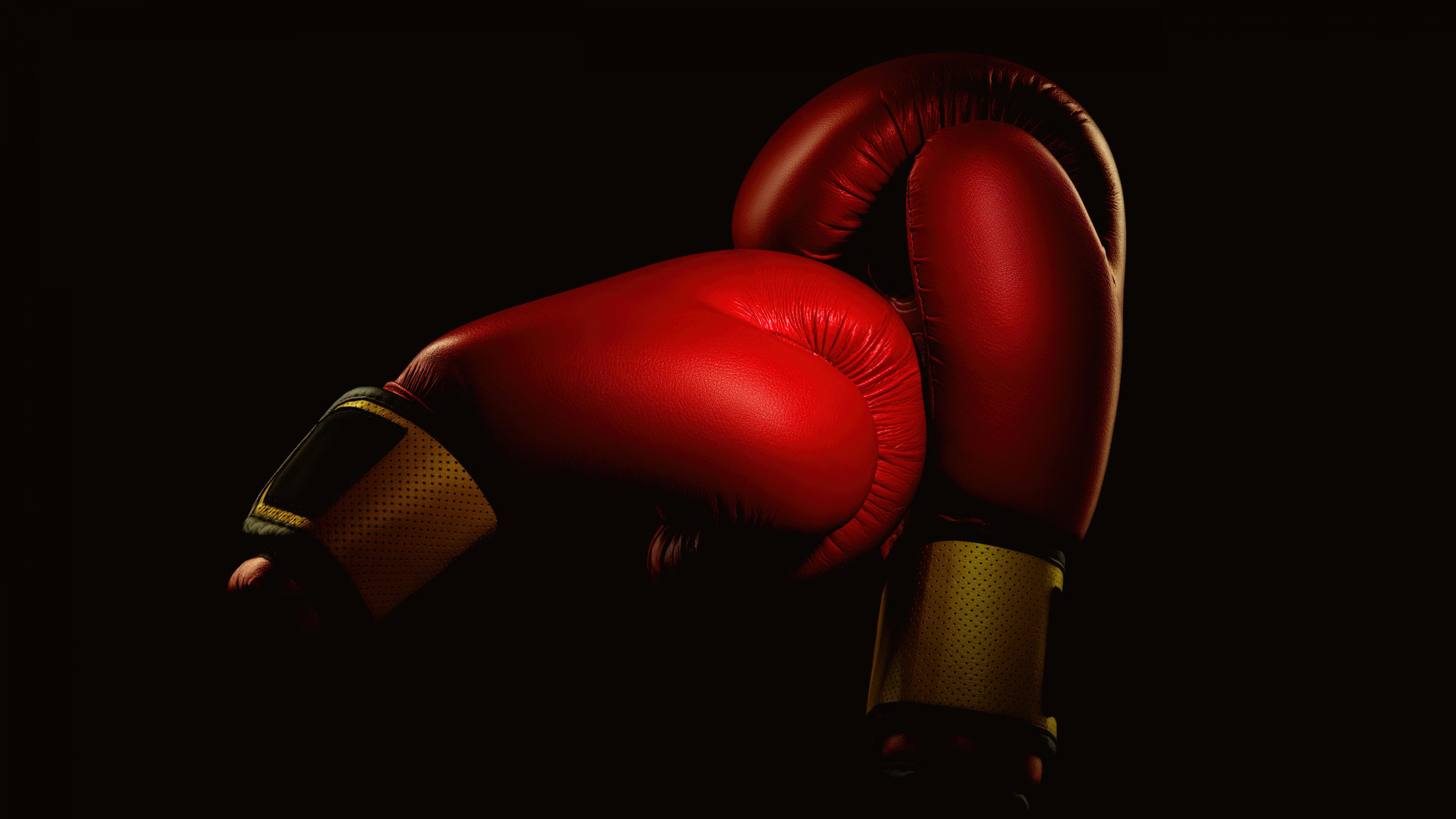 A pair of boxing gloves with vibrant red highlights and dramatic lighting against a dark black background.