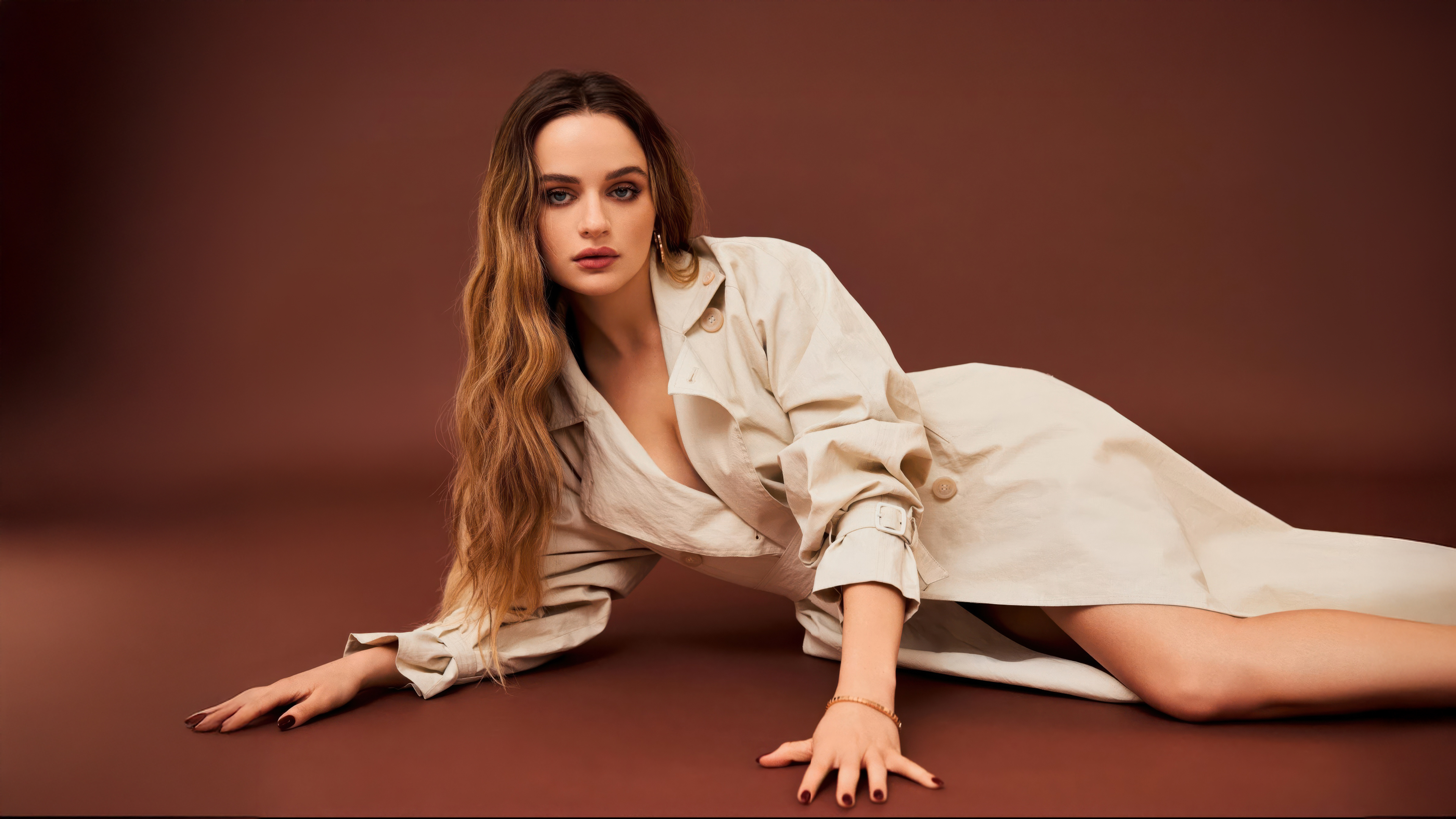 A glamorous professional studio portrait of actress Joey King posing against a solid brown background.