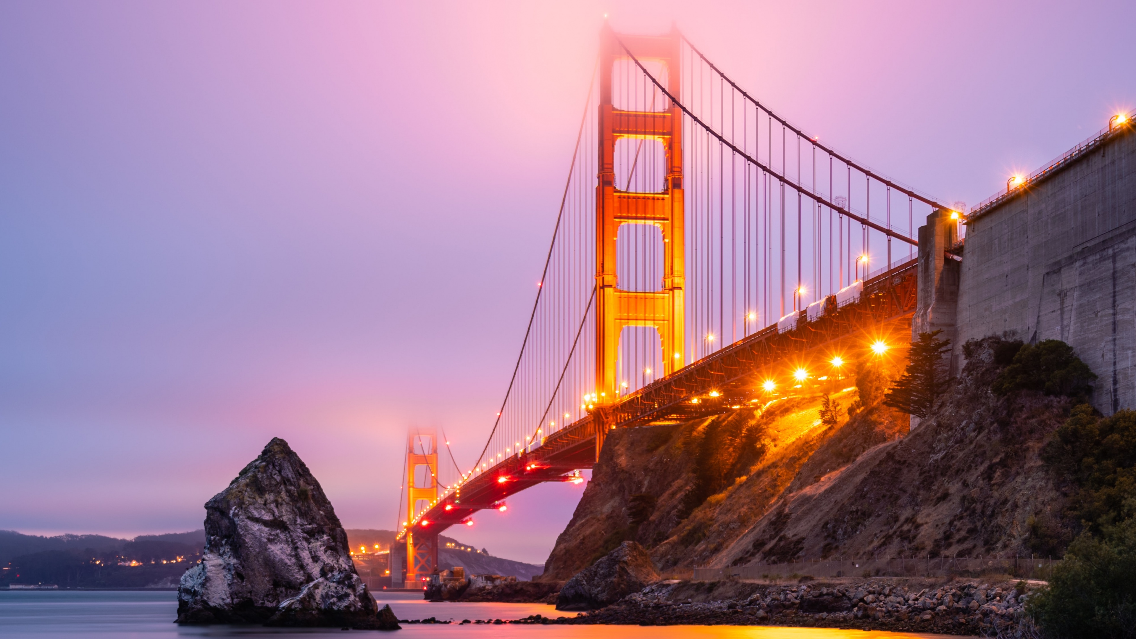 The Golden Gate Bridge in San Francisco under a pink sunset sky with atmospheric fog and bridge lights.