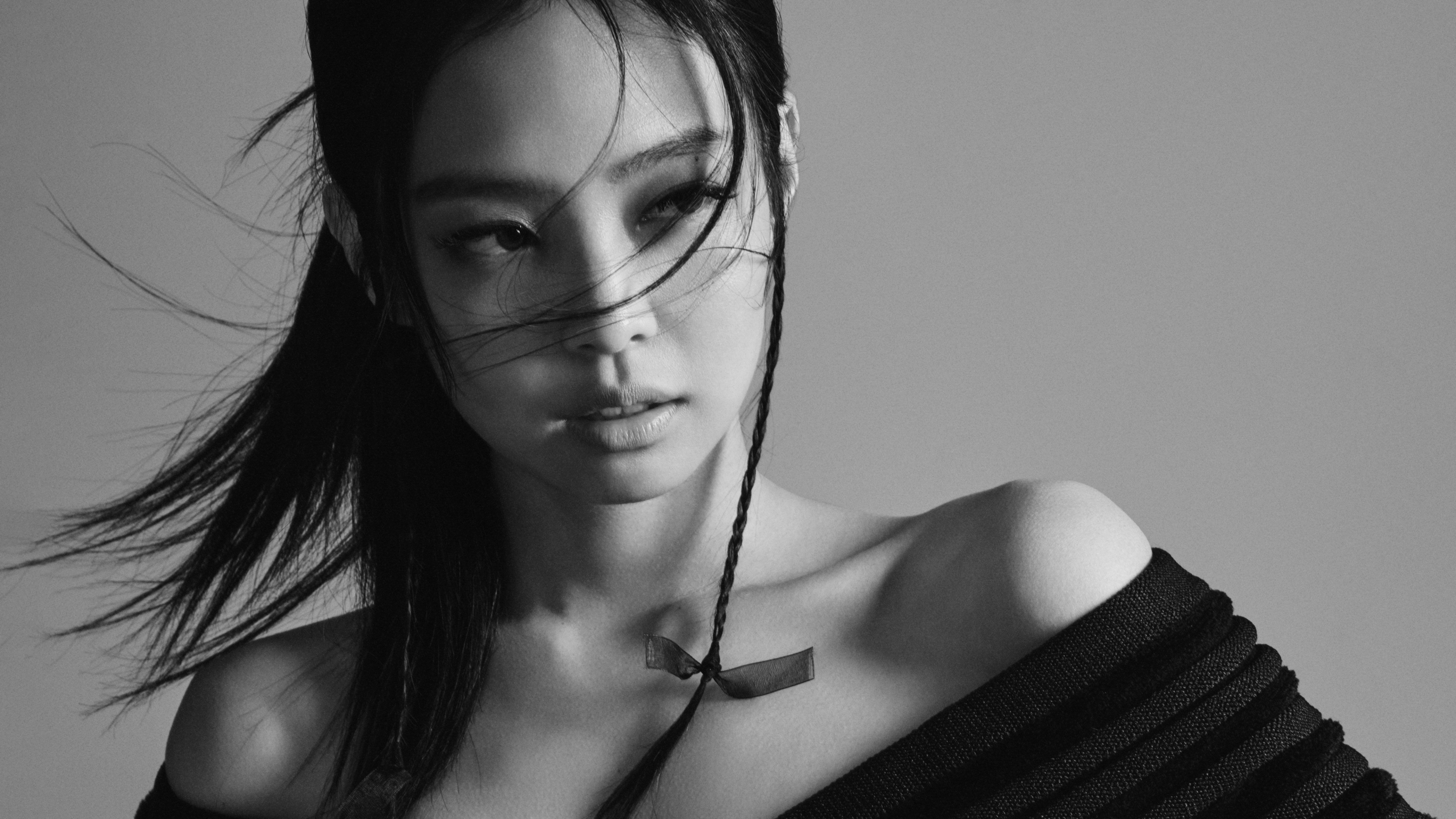 A high-resolution black and white portrait of South Korean singer Jennie Kim against a grey background in a monochrome photography style.