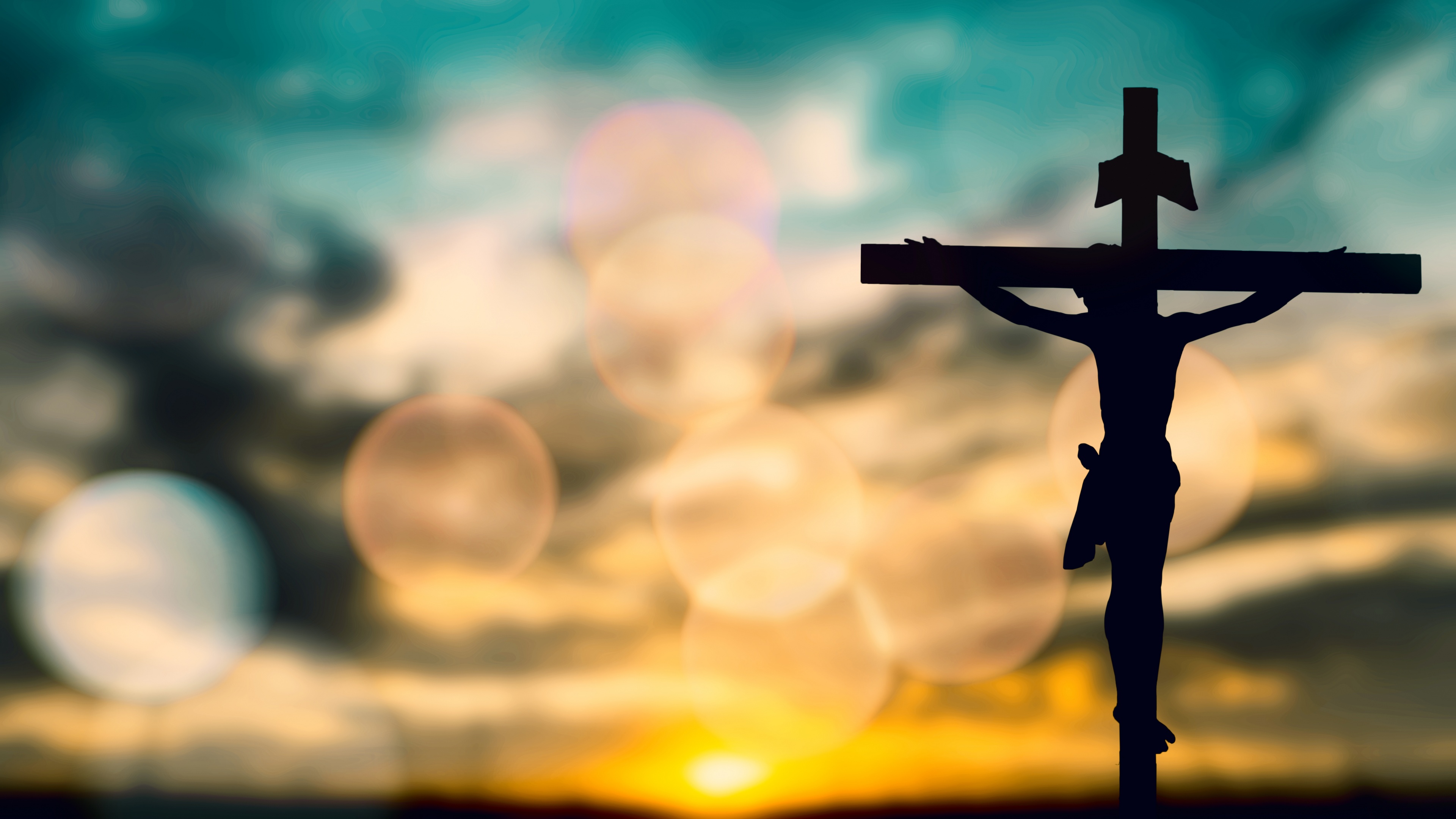 A striking silhouette of the Christian cross positioned against a vibrant sunset with warm orange and gold tones.