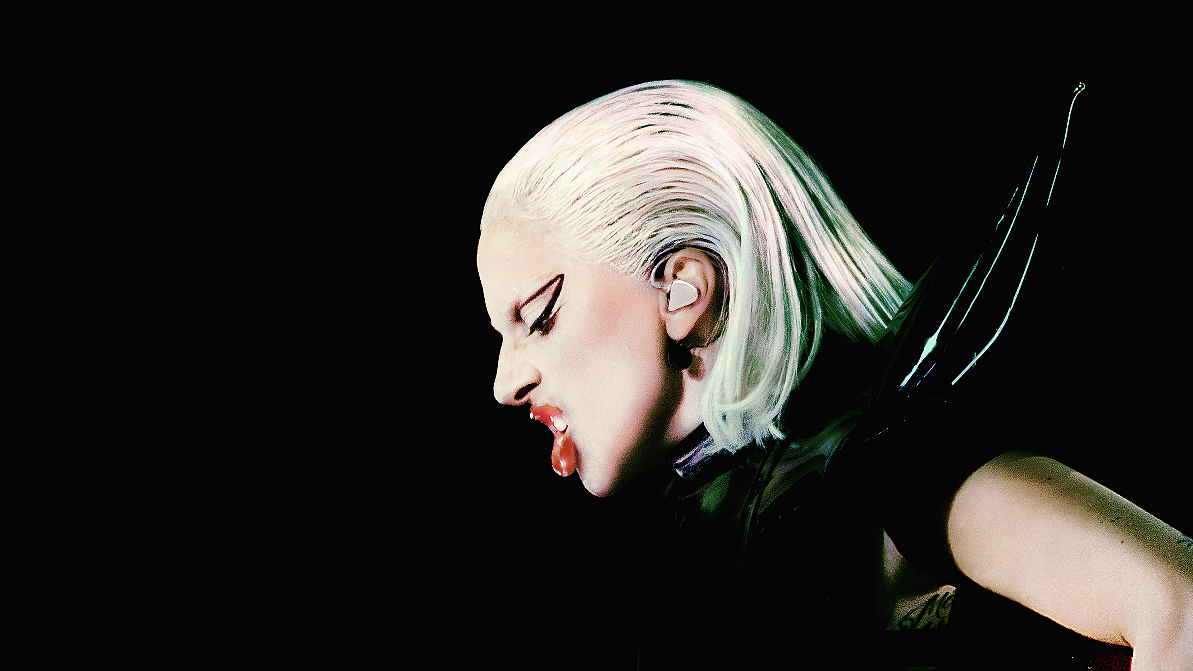 Lady Gaga performing on stage during a live concert against a dark black background.