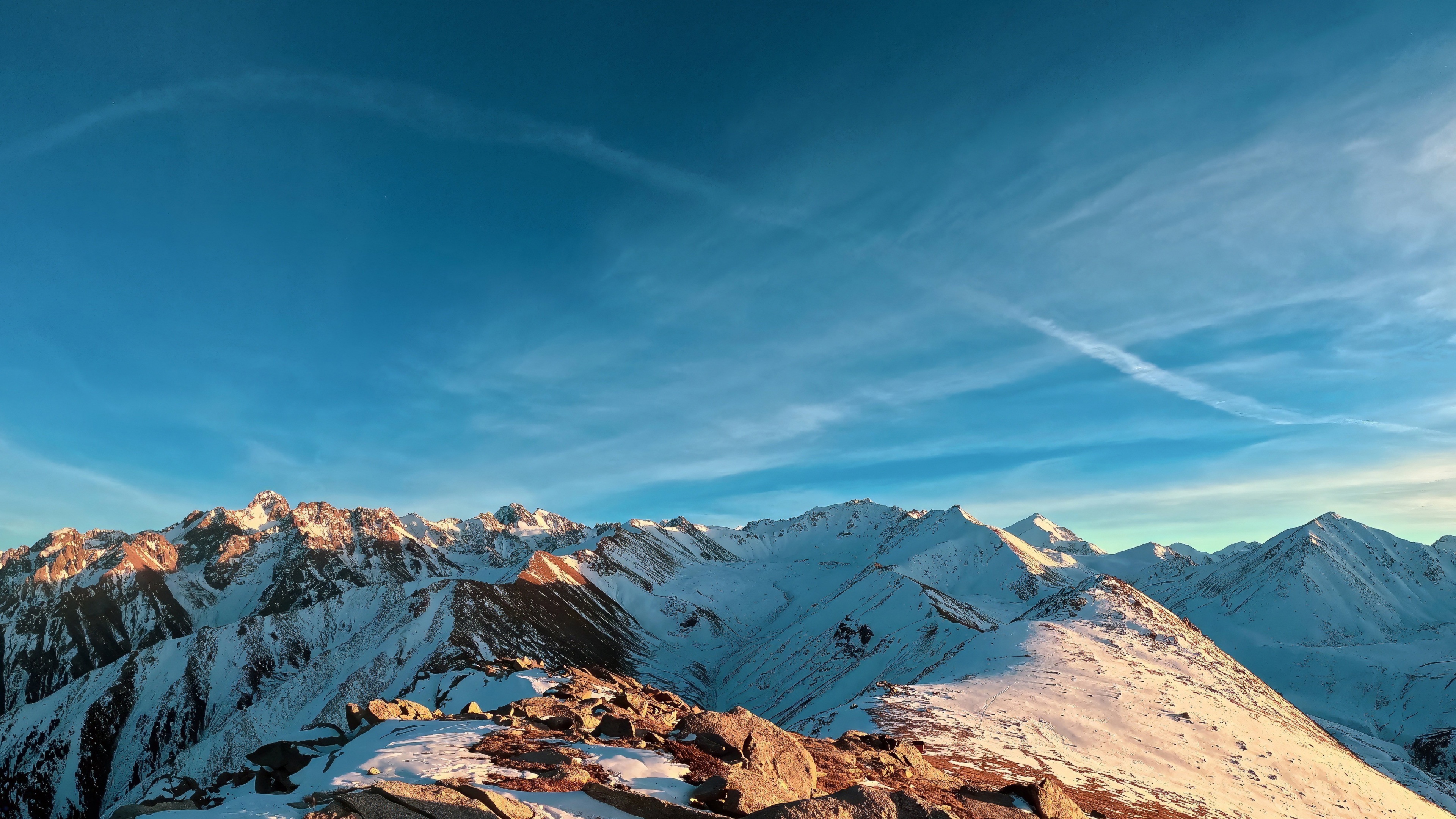 A wide panoramic shot of snow-capped mountains under a bright blue sky on a sunny day.