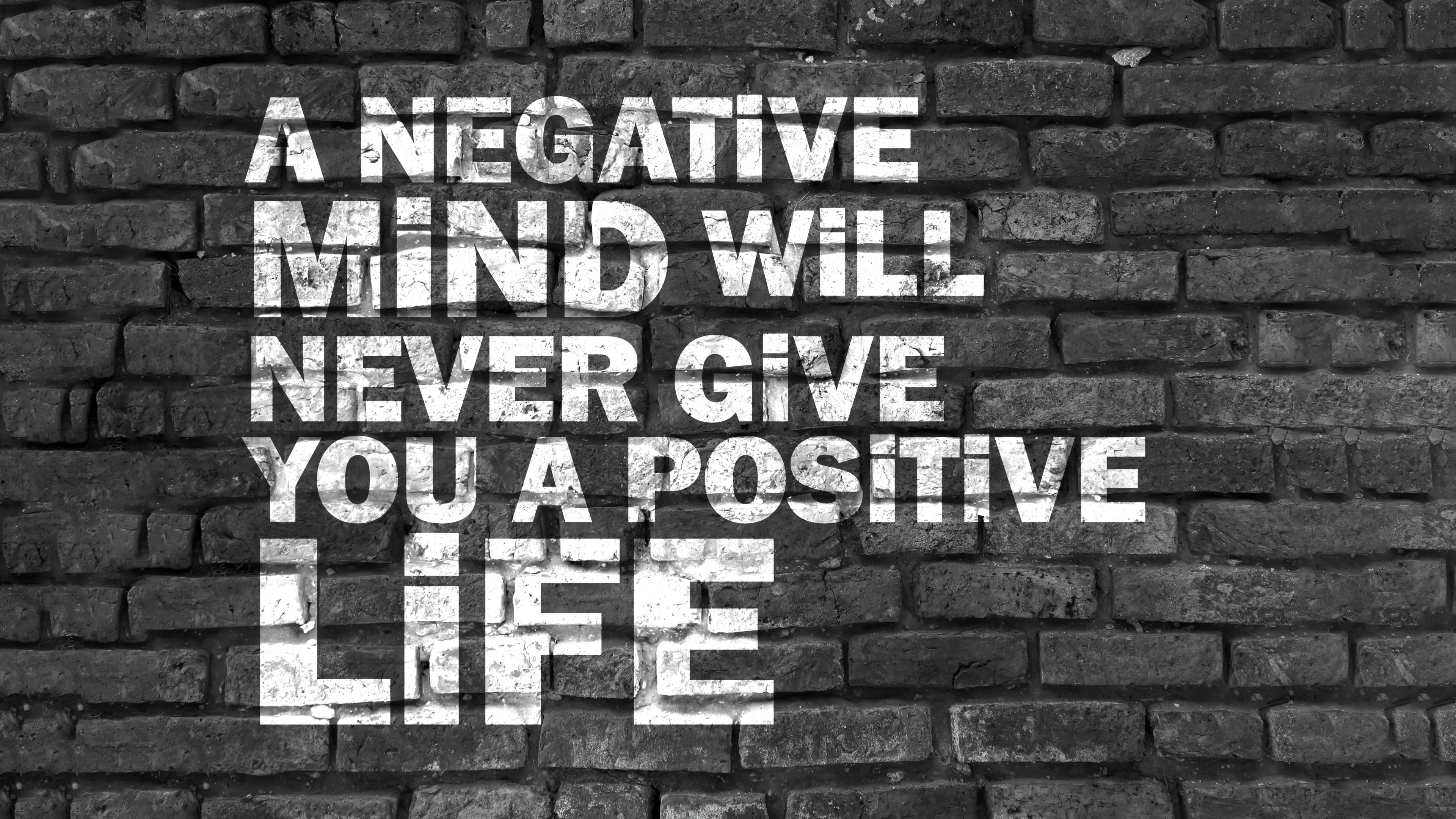 A black and white close-up of an inspirational positivity quote on a rugged brick wall.