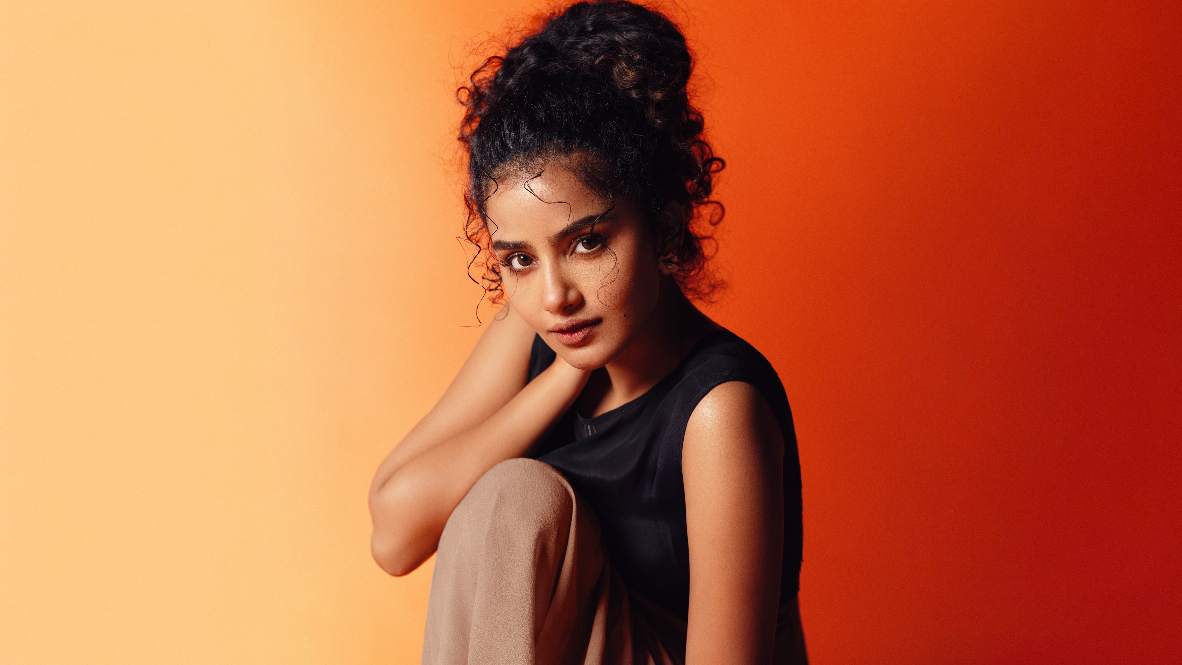 Anupama Parameswaran posing against a bright orange backdrop in high resolution