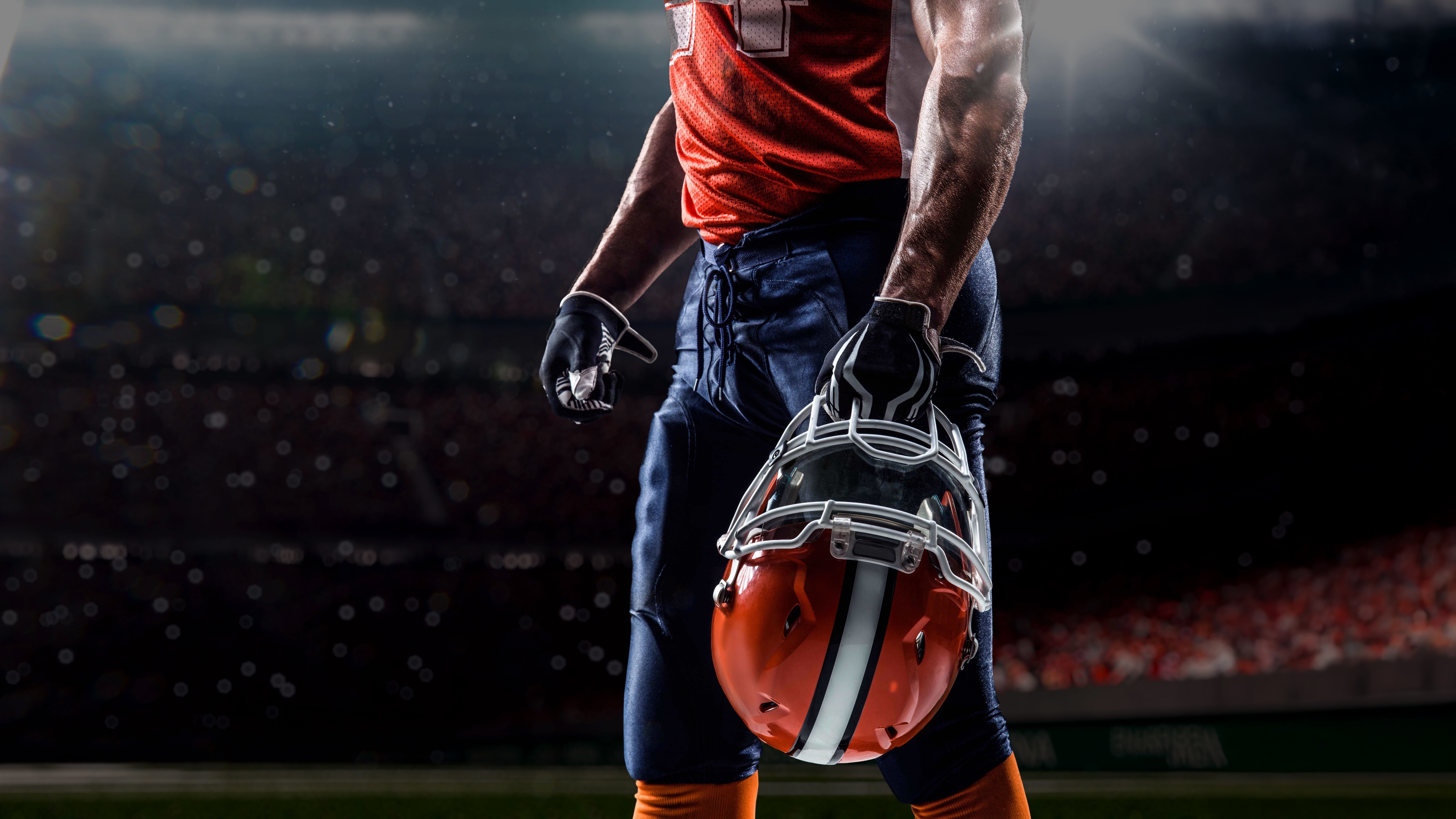 A close-up view of an American football player wearing a helmet, set against the backdrop of a massive, illuminated stadium.