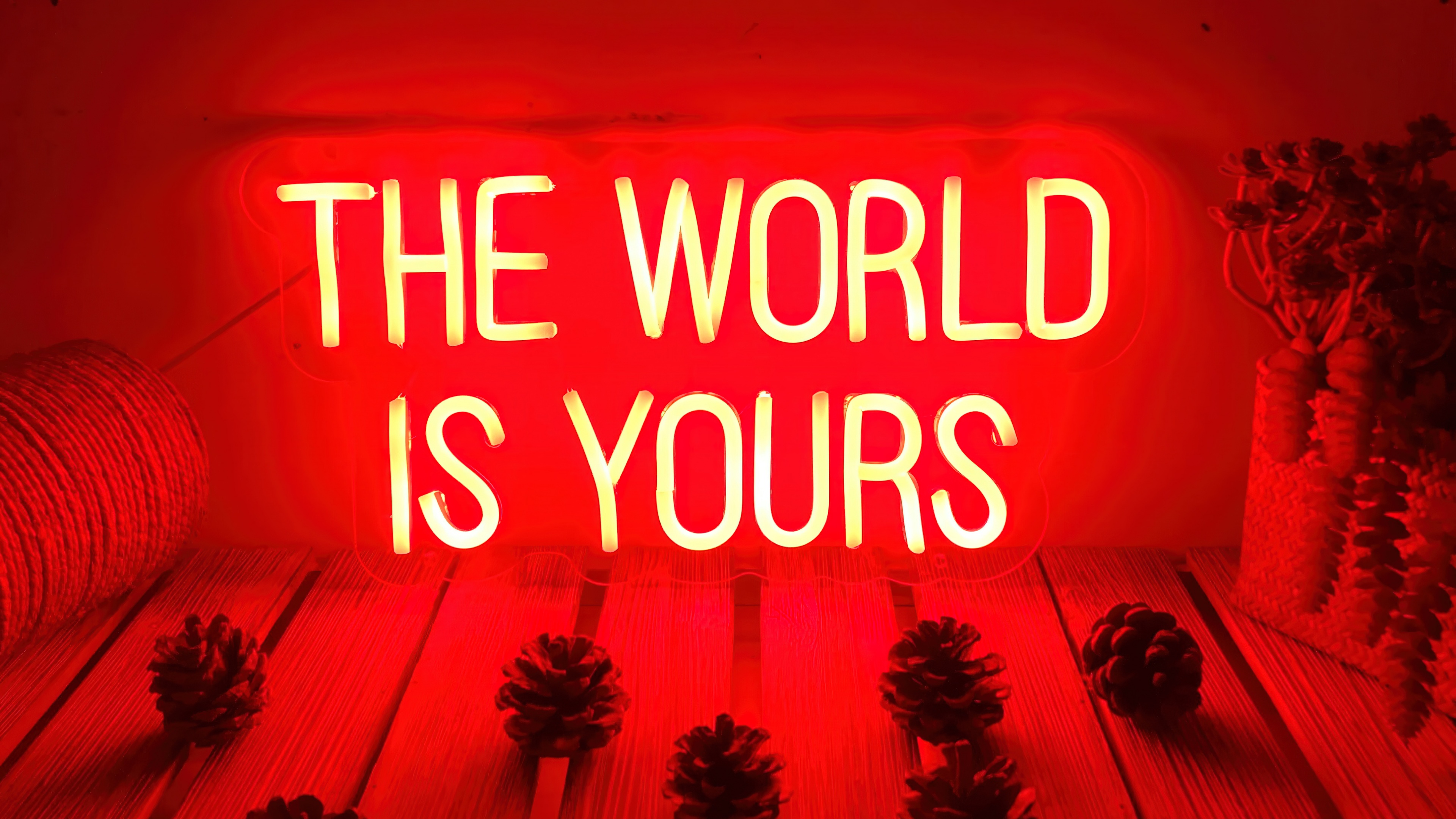 A vibrant red neon sign displaying the text 'The World is Yours' against a dark, atmospheric background with a red color palette.