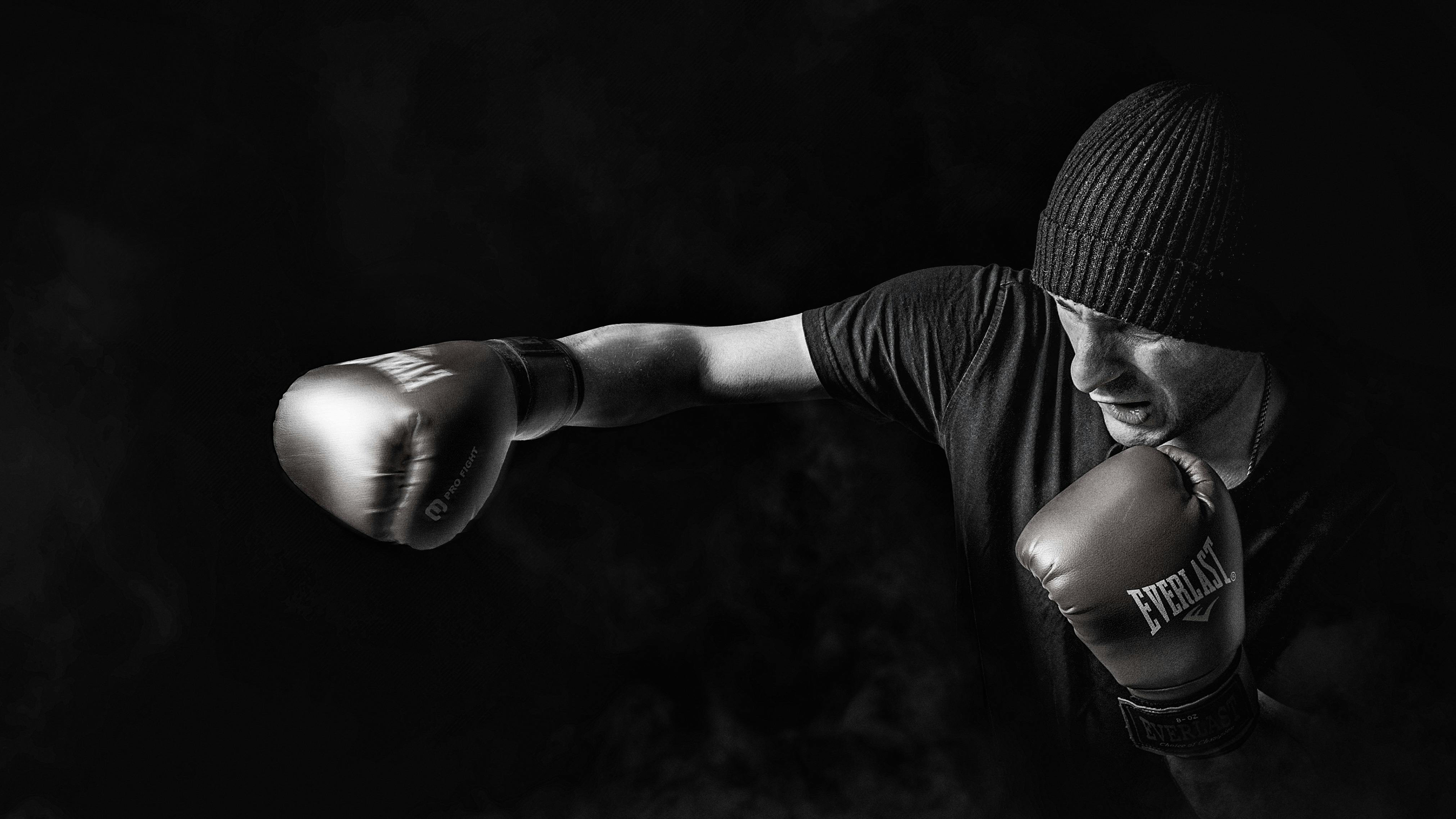 A high-contrast, black and white close-up of a boxer wearing gloves against a dark, moody background.