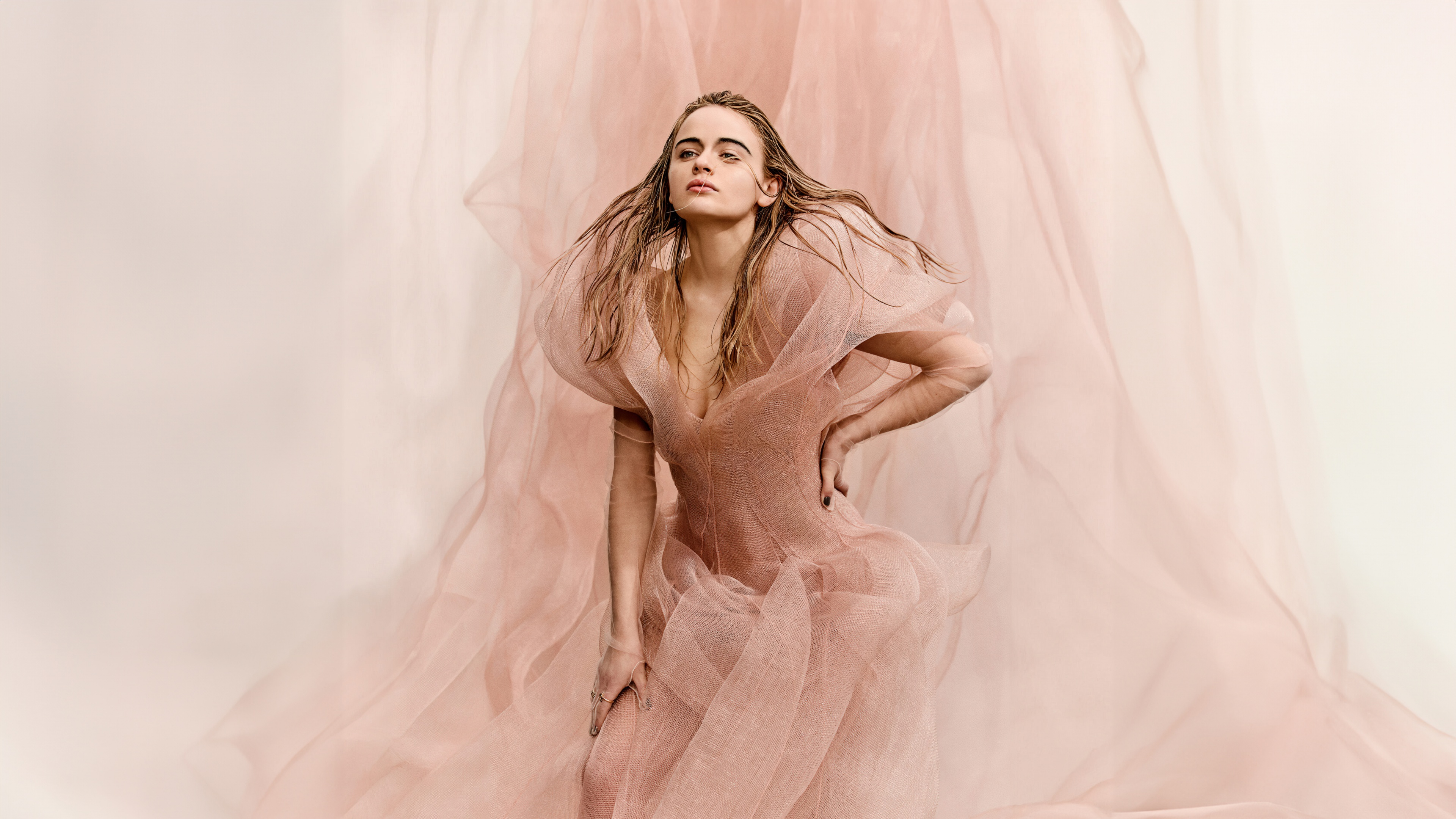 A close-up portrait of actress Joey King with a soft peach background.