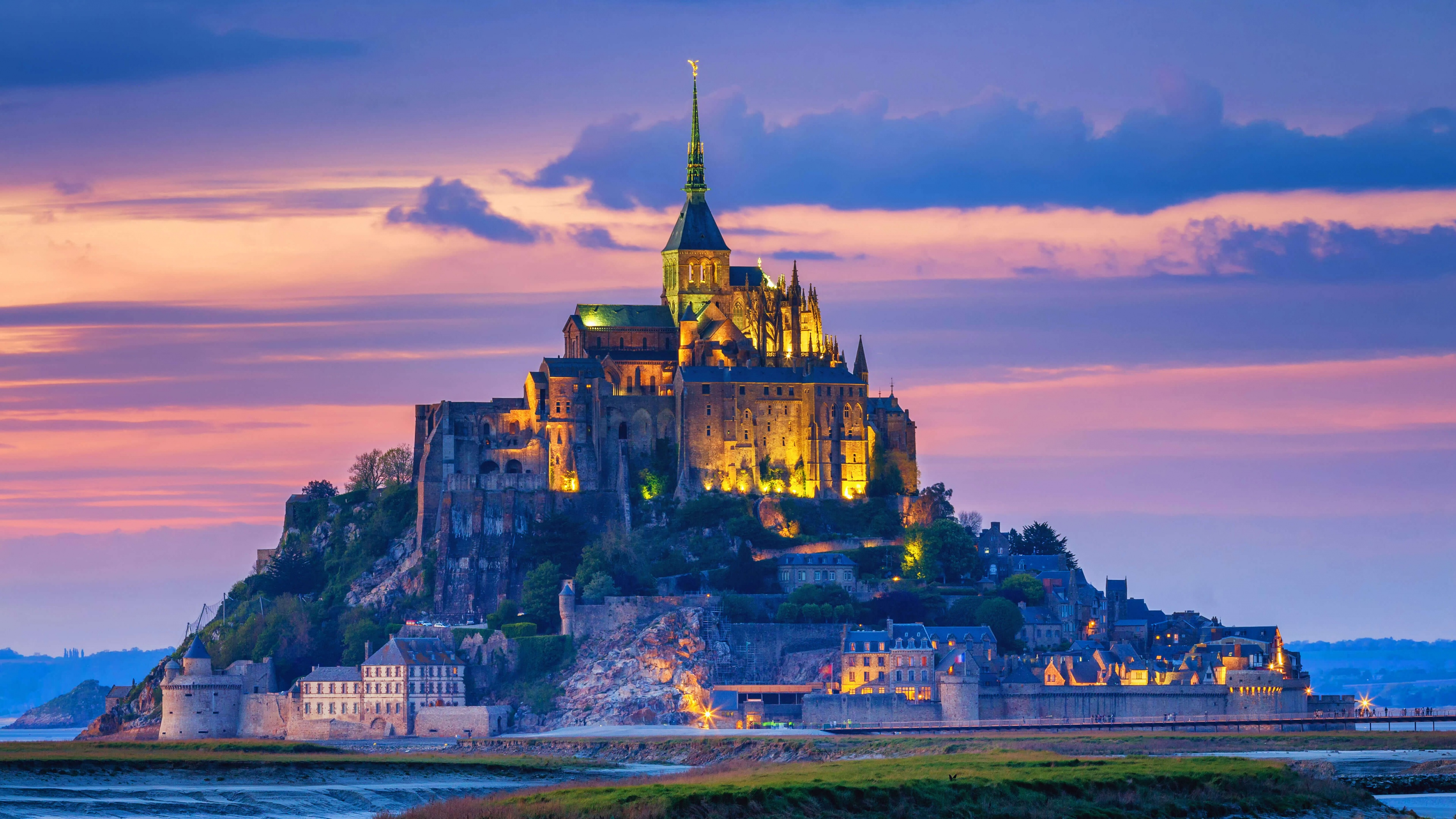 A panoramic view of the ancient Mont Saint-Michel abbey in Normandy, France, during a colorful evening sunset.
