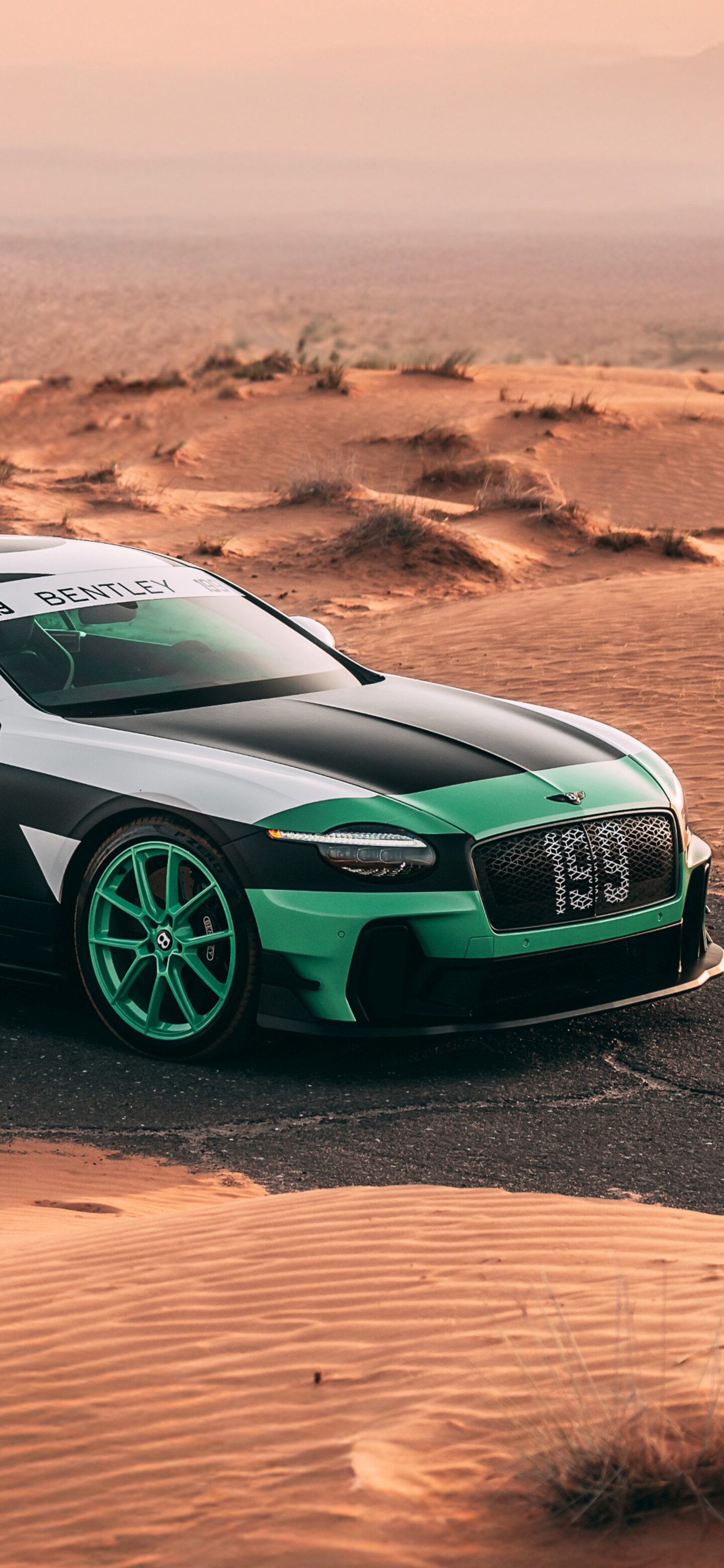 A striking green Bentley Continental GT Supersports parked in a wide desert landscape under bright sunlight.