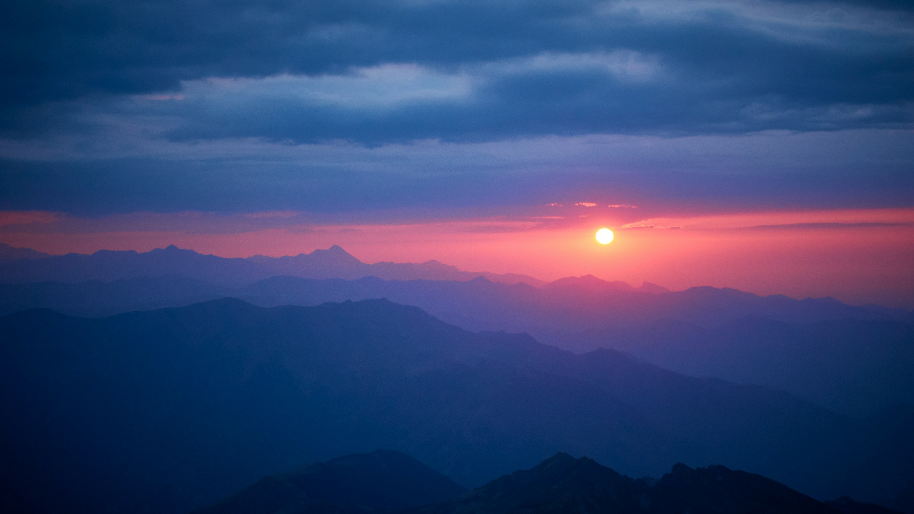 A breathtaking view of a mountain range in France during a vibrant sunset with golden light hitting the peaks.