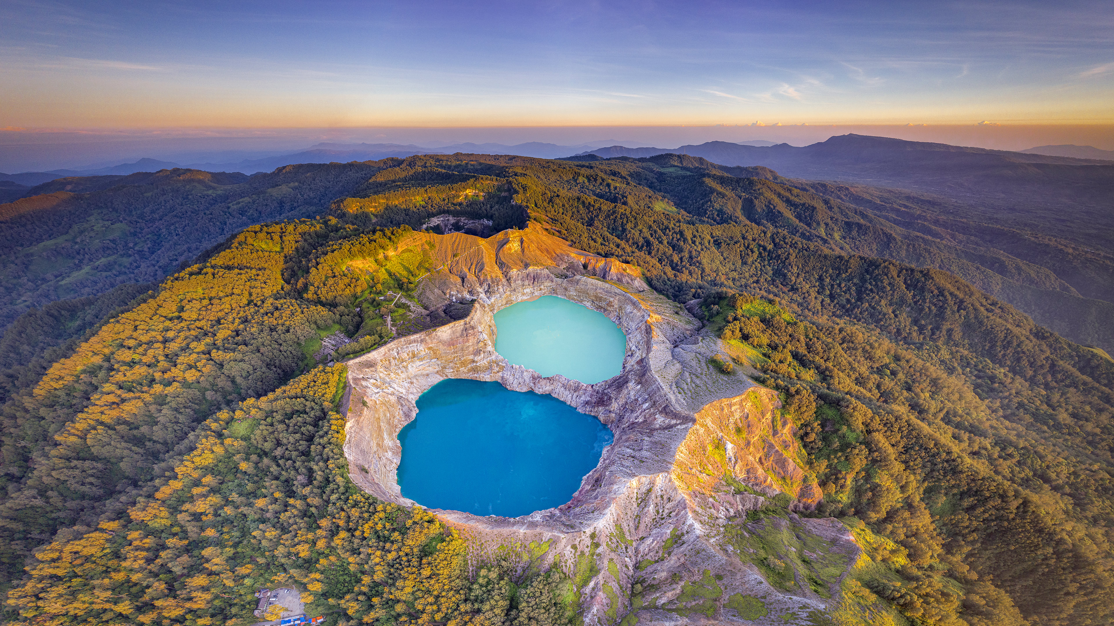 An aerial drone view of a serene blue volcanic crater lake surrounded by dense green tropical forests in Indonesia.