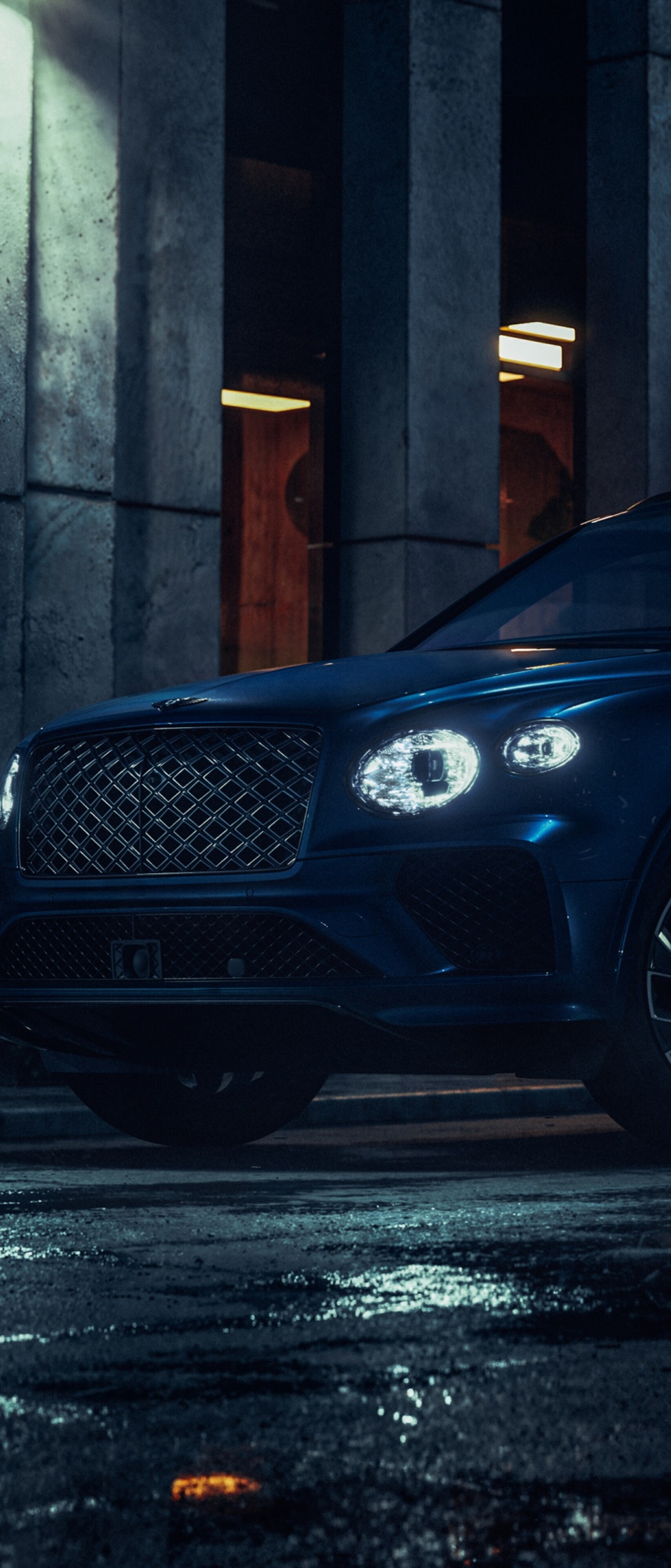 The 2026 Bentley Bentayga EWB driving through a dark, modern city street illuminated by glowing urban lights and neon reflections.
