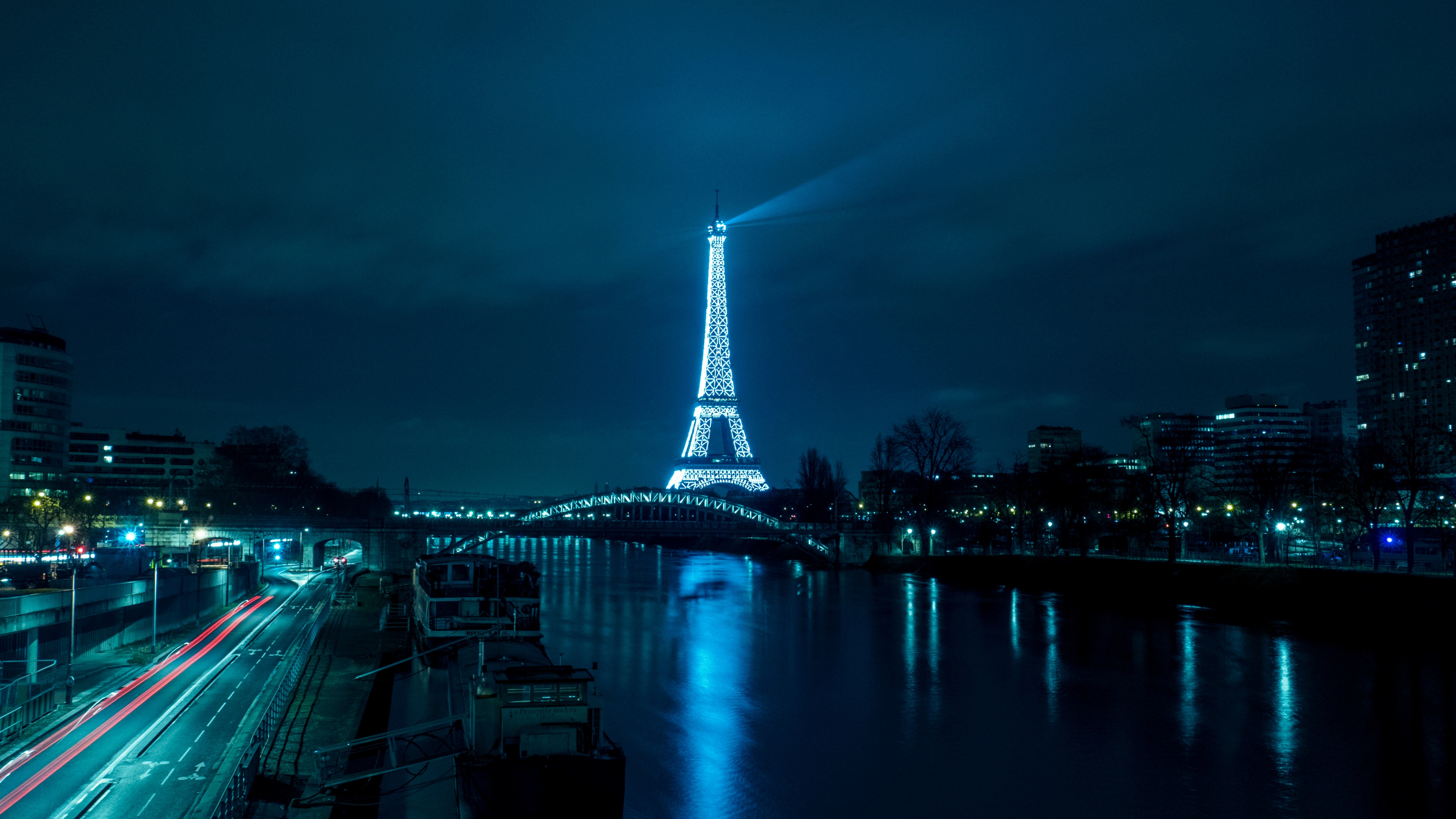The illuminated Eiffel Tower at night in Paris with colorful city lights reflecting on the river water.