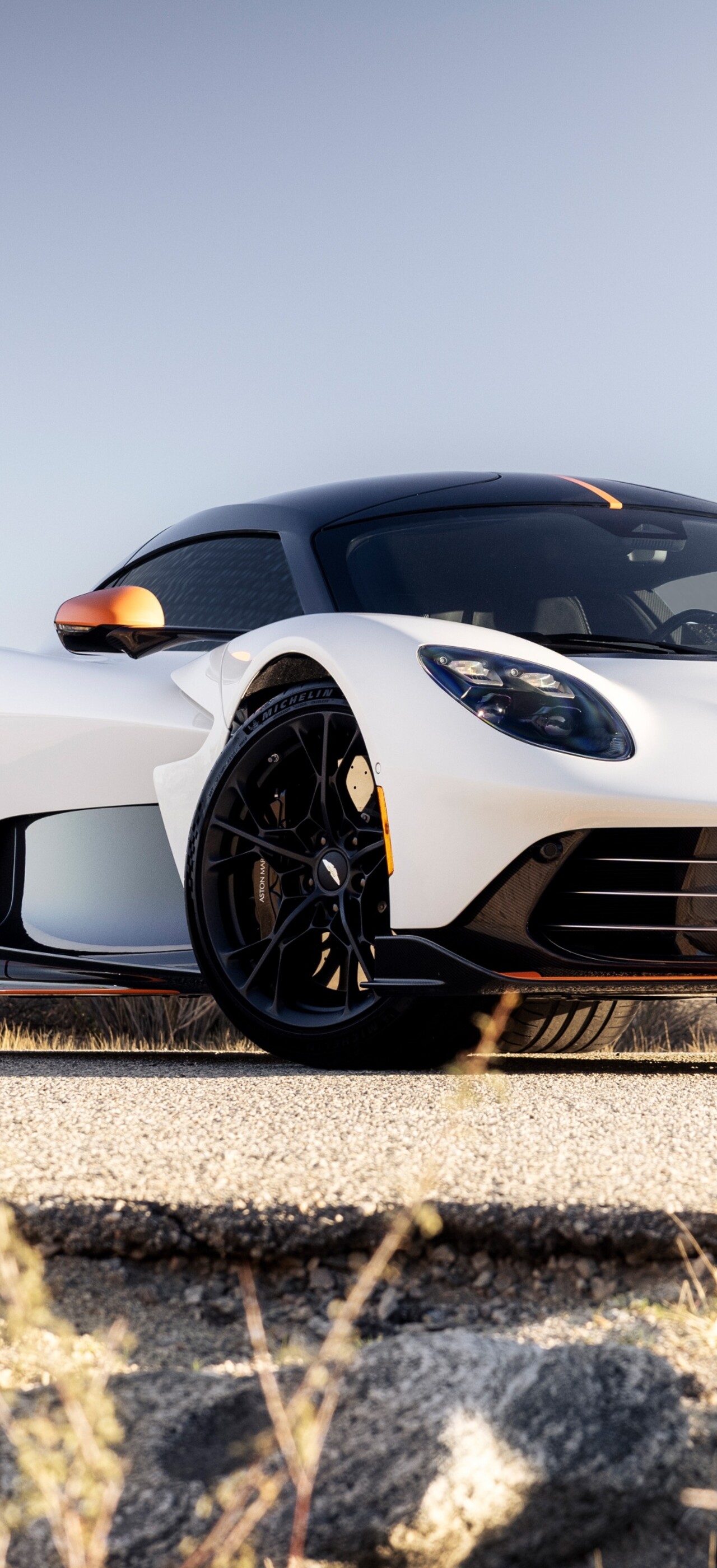 A pristine white Aston Martin Valhalla plug-in hybrid supercar driving through a vast desert landscape with golden sand dunes.